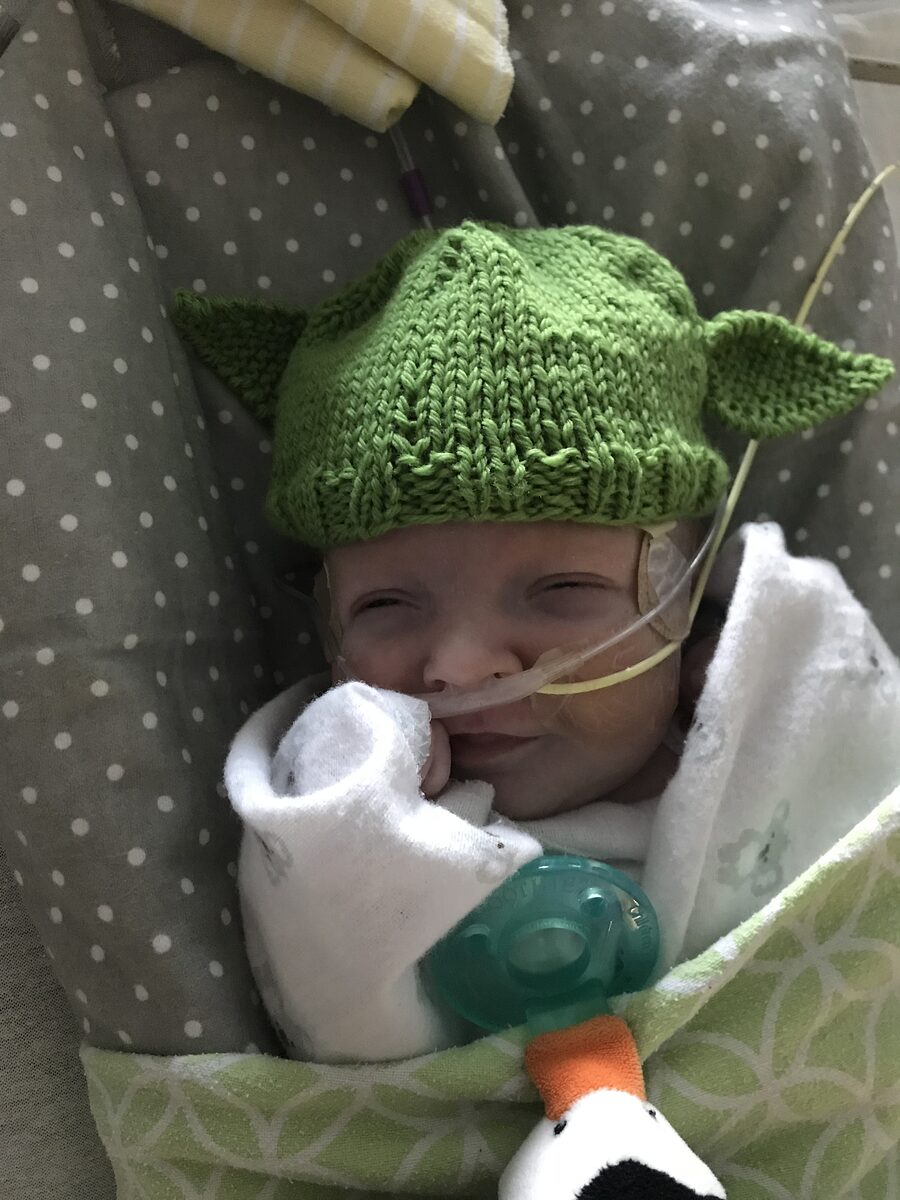 Newborn baby with oxygen and feeding tube wearing a hand-knit Yoda hat.